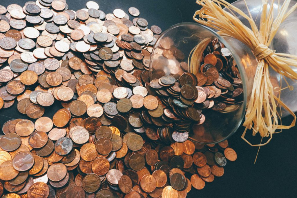 Copper pennies spill out of a large glass jar onto a black surface.
