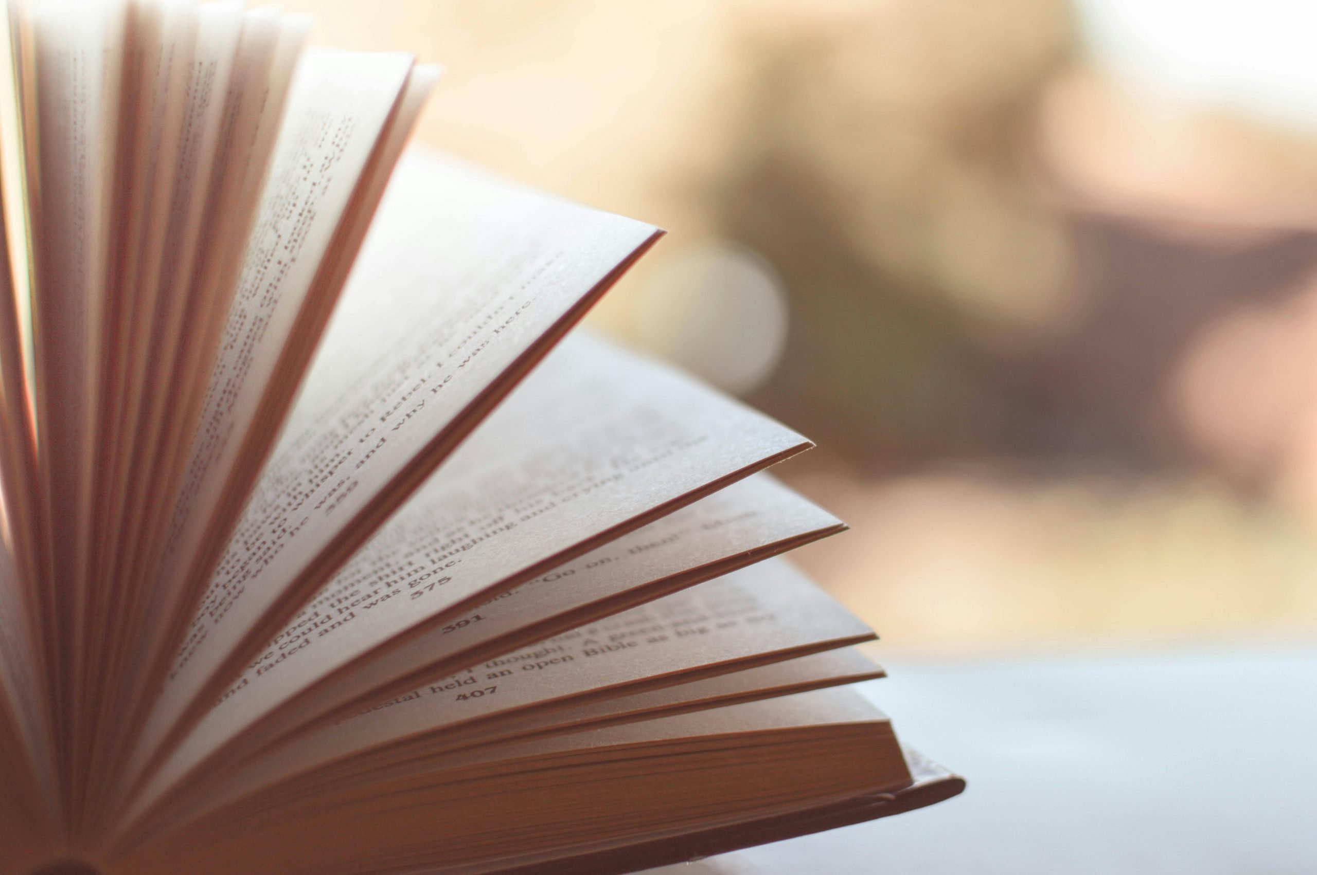 A book face up on a table. Pages of the book are open and look like they're flapping in the wind. The book is on a grey desk with a blurry background.