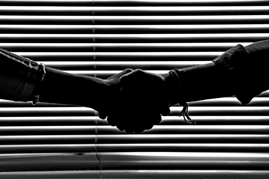 Black and white image of two hands shaking against a horizontally striped wall.