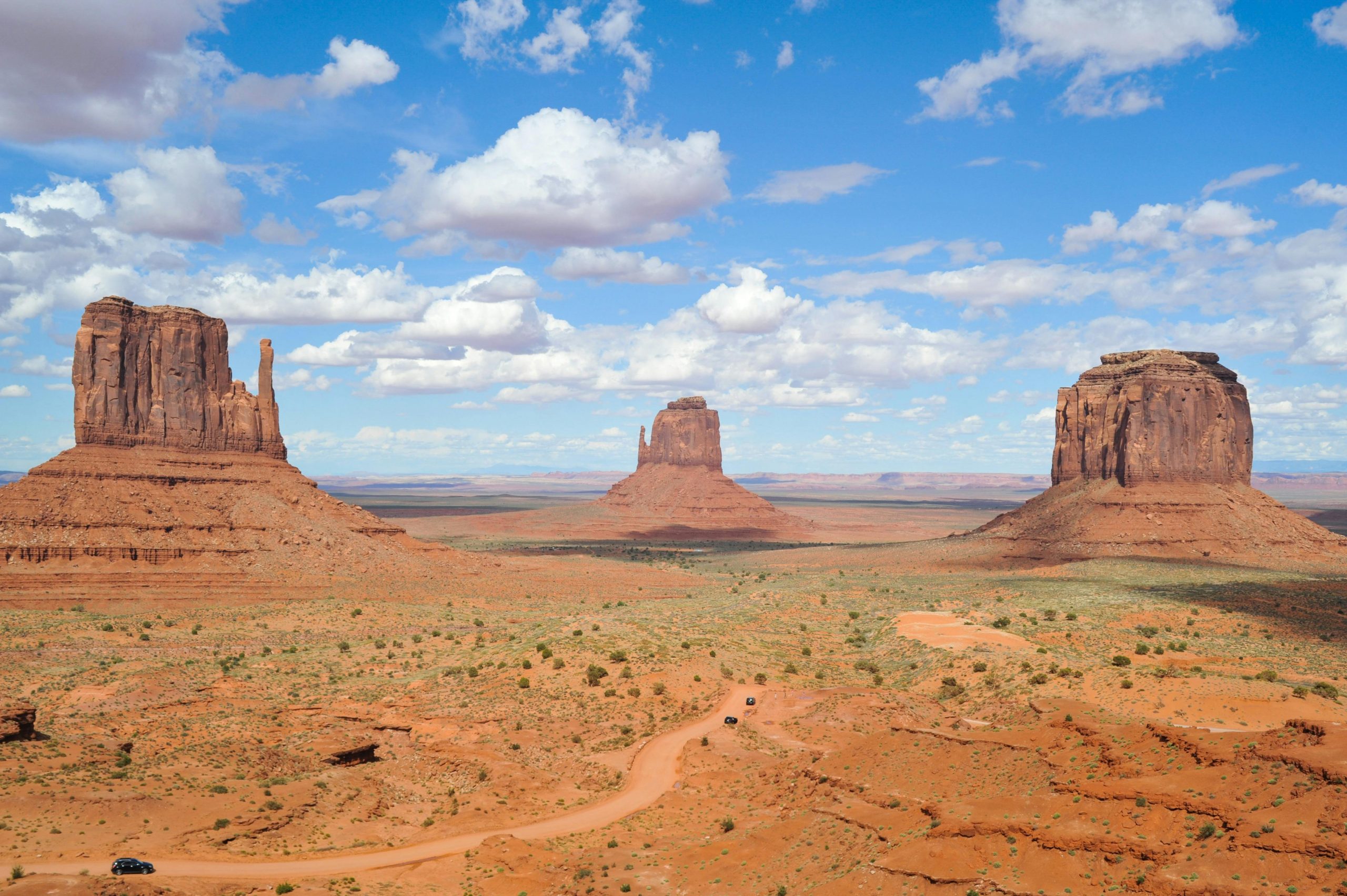 An orange barren landscape in America. Looks like the Wild West, with large rocks, small green bushes and tumbleweed.