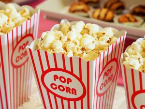 A red and white striped popcorn box with a scalloped edge. The box is full of yellow buttery popcorn.