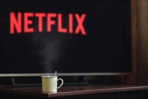 The Netflix logo on a large television screen. The television screen is out of focus and a yellow coffee mug sits in front of the television in focus.