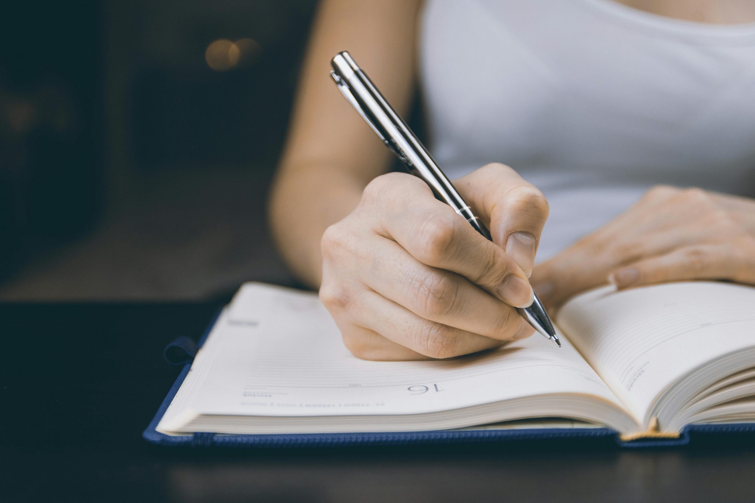 A woman writes in a notebook with a silver pen.
