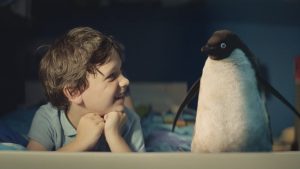 A snapshot of the John Lewis Christmas advert. A boy is laying in bed with his pet penguin next to him.