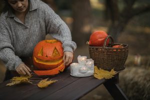 A woman carves a pumpkin on a dark wooden bench outside.