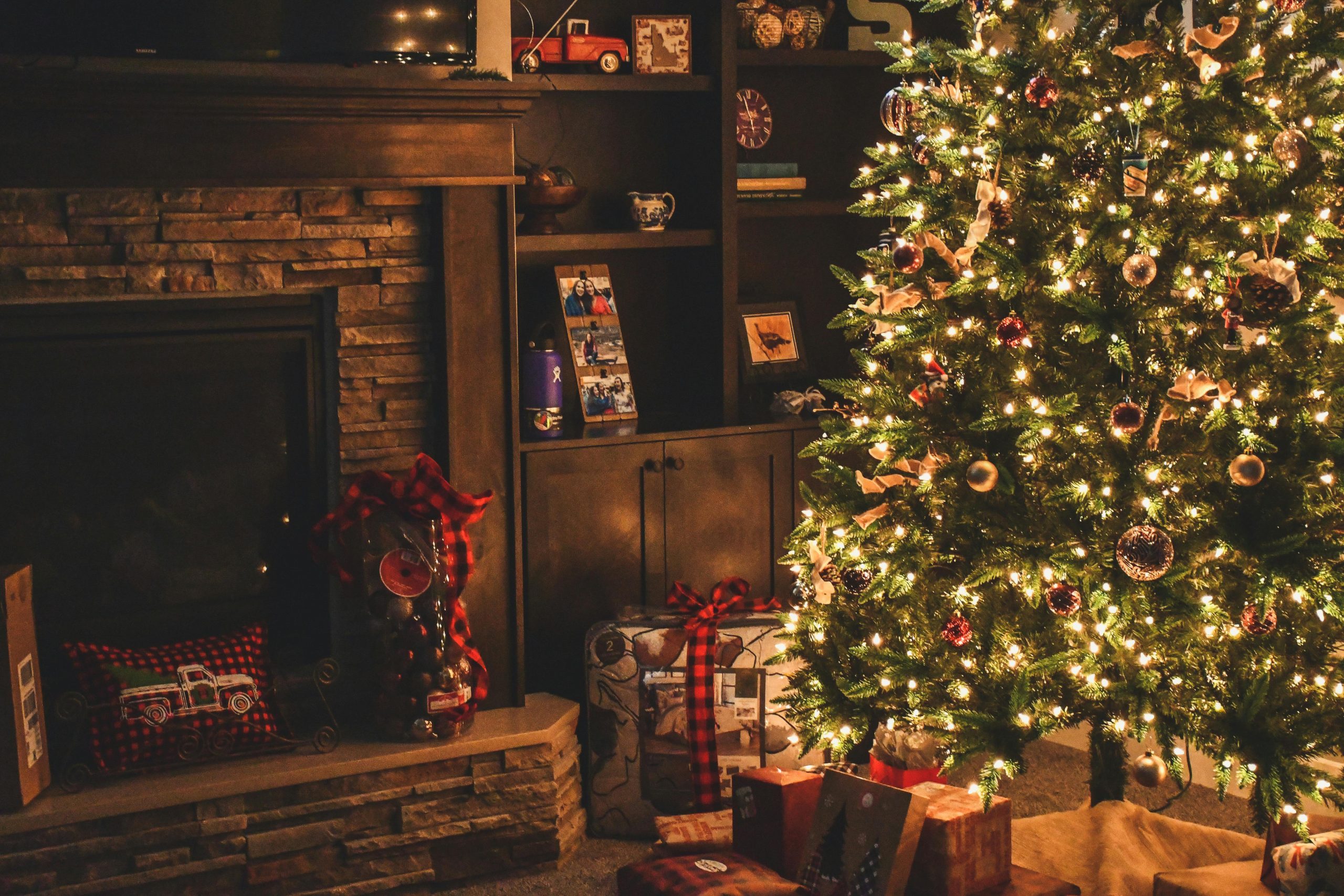 A festive living room with a red brick fireplace in the centre, a Christmas tree to the right and a presents over the floor.