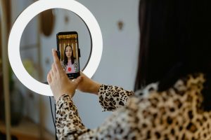 Woman in leopard print blouse holds a black iPhone in front of a bright ring light.